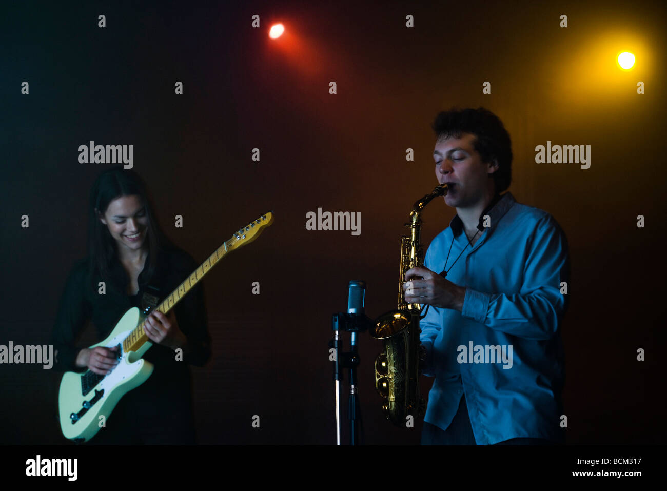Young musicians playing electric guitar and saxophone in night club Stock Photo