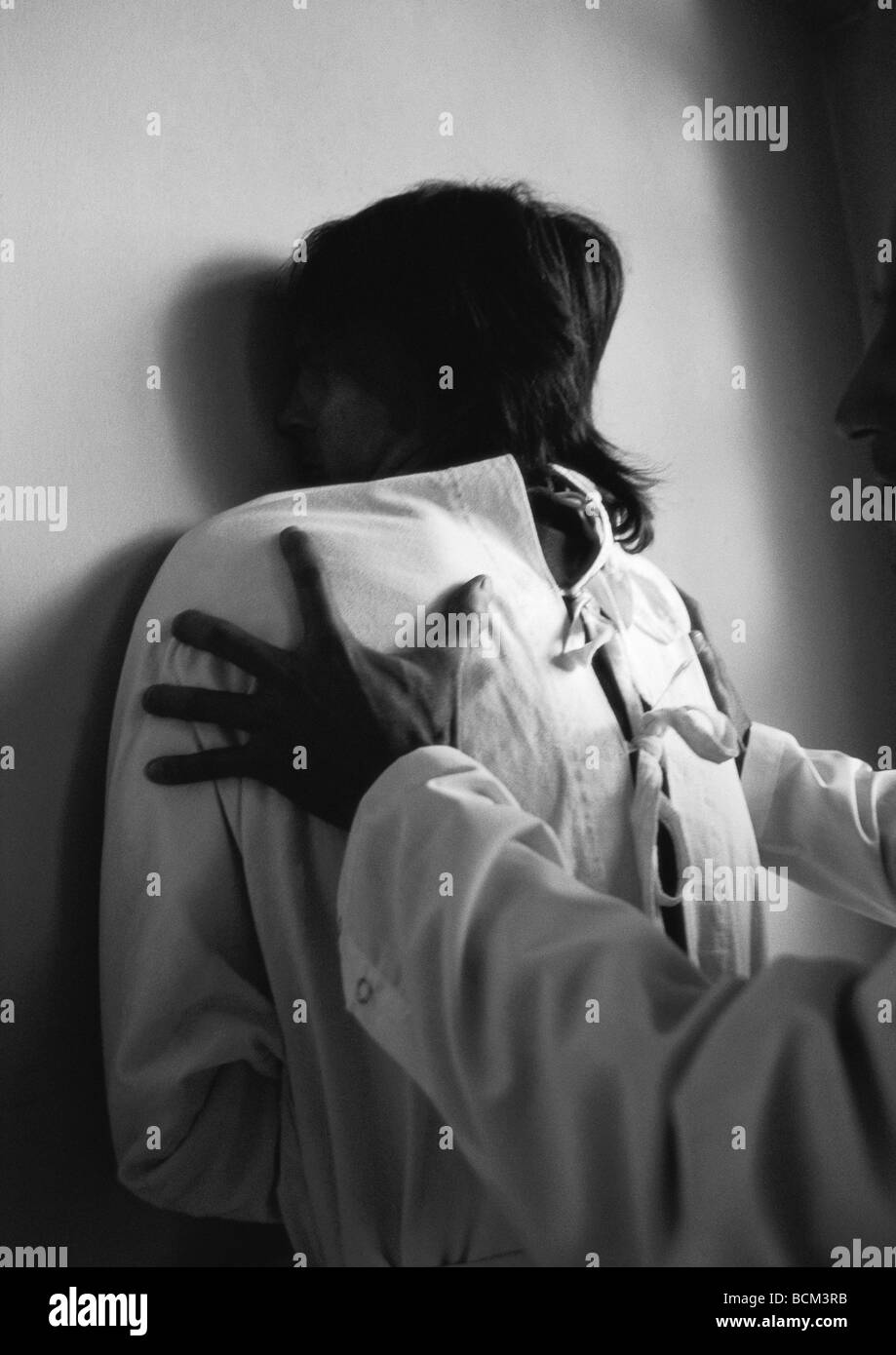 Orderly holding man in straitjacket against wall Stock Photo