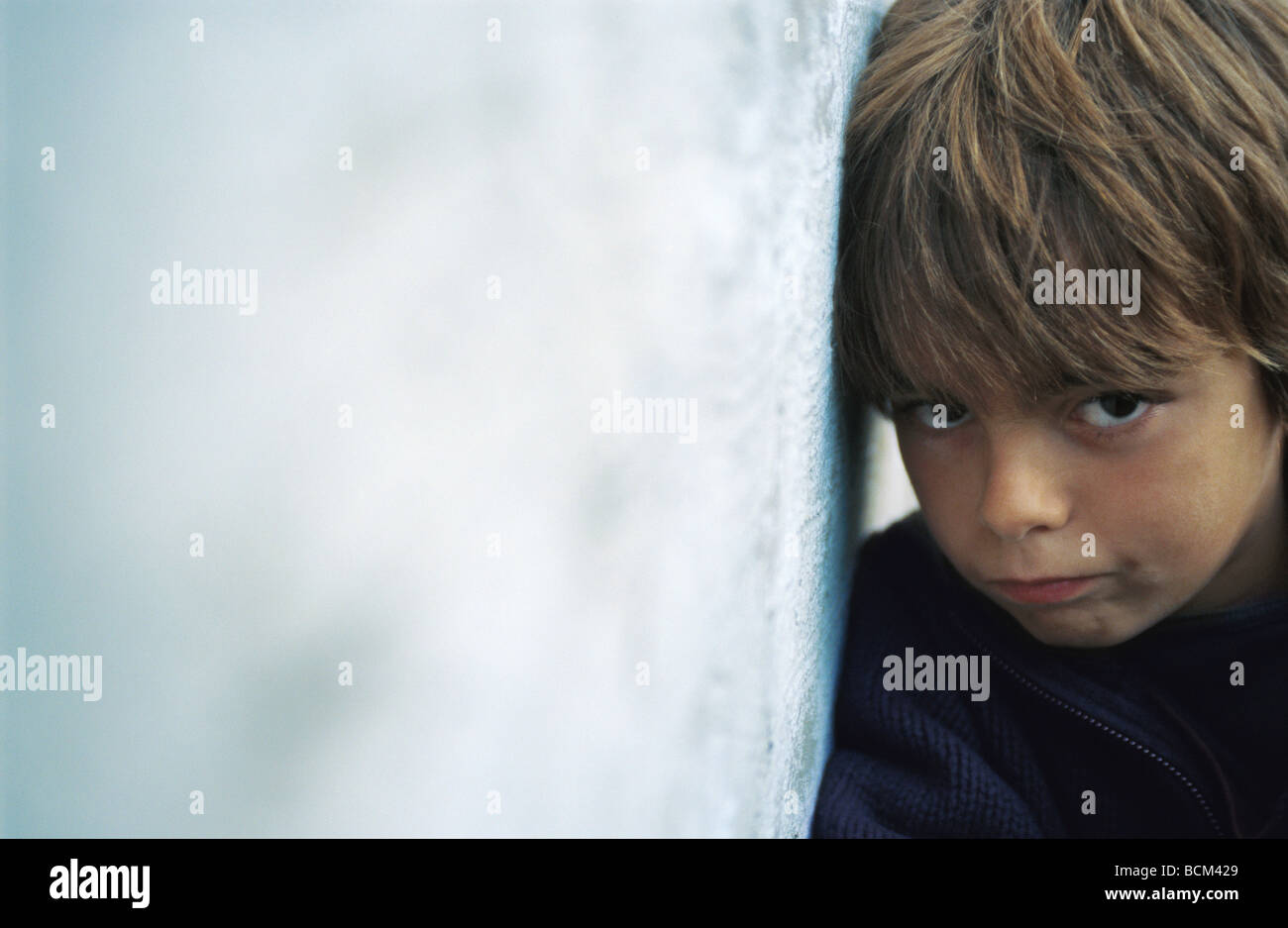 Boy leaning against wall, frowning at camera Stock Photo