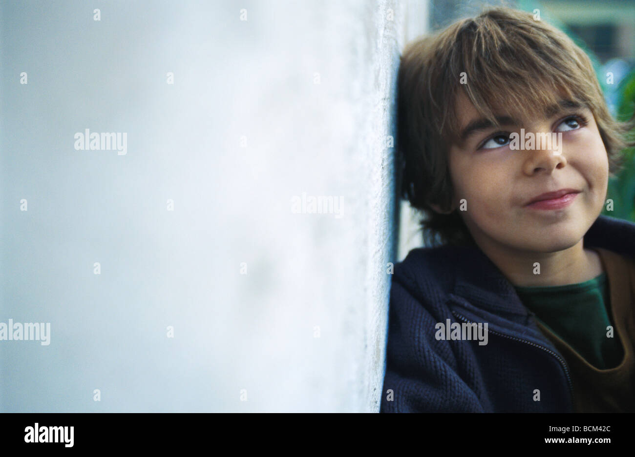 Boy leaning against wall, smiling Stock Photo