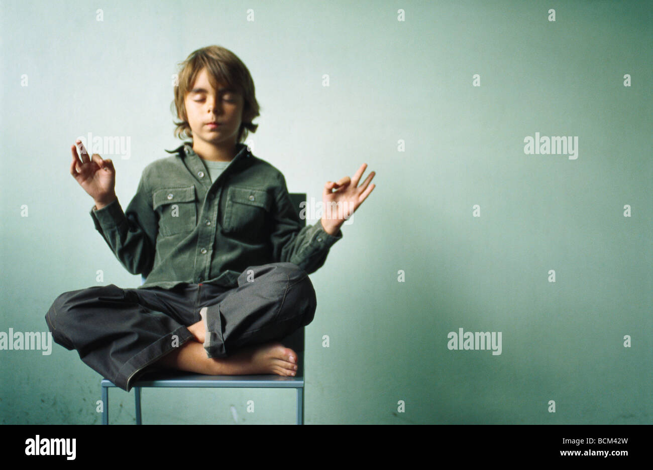 Boy sitting in lotus position in chair, eyes closed Stock Photo Alamy