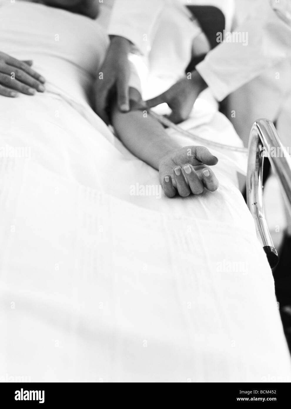 Patient lying in hospital bed, doctor adjusting IV drip Stock Photo