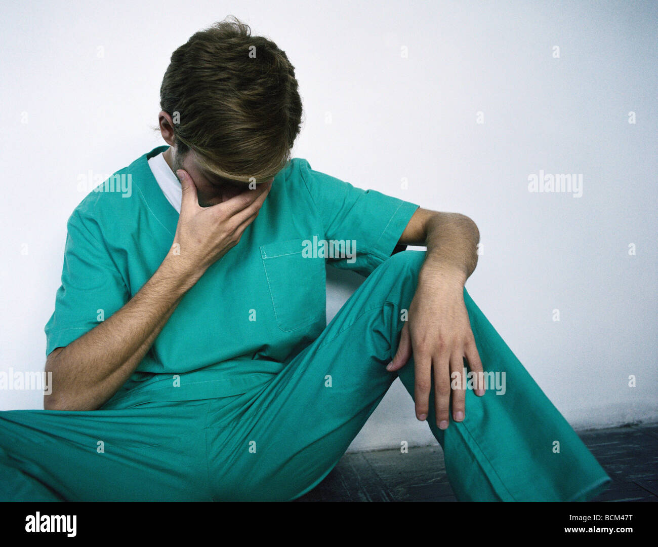 Man in hospital scrubs sitting on the floor with head down and hand
