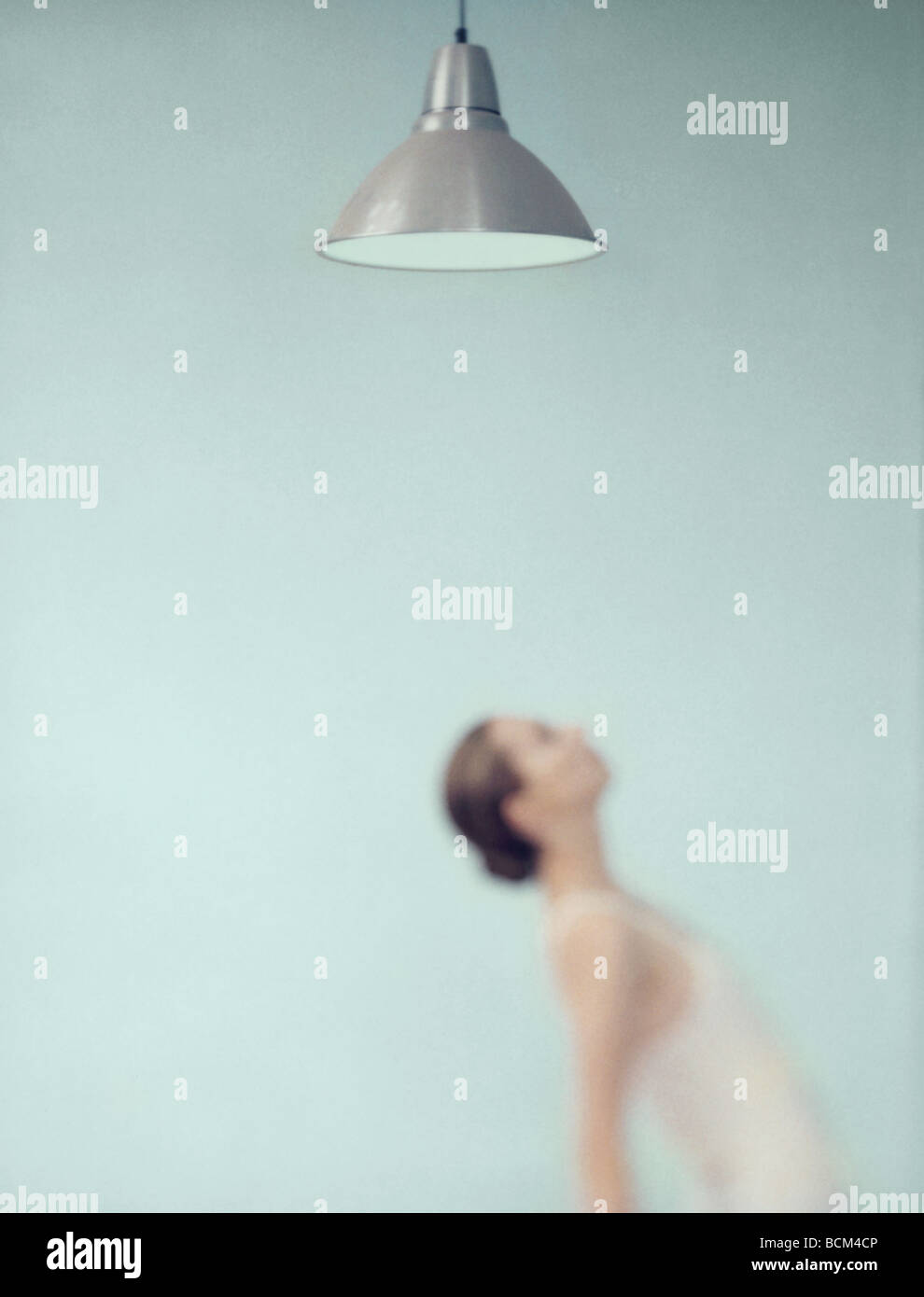 Young woman bending over backwards under ceiling lamp, focus on lamp in foreground Stock Photo