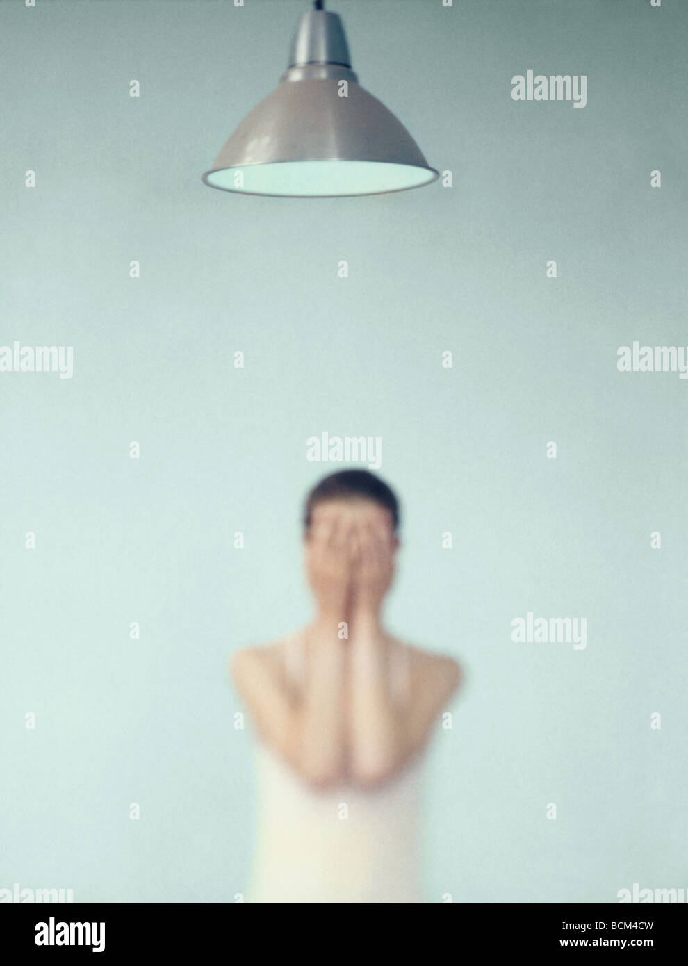 Young woman standing with hands over face, focus on lamp in foreground Stock Photo