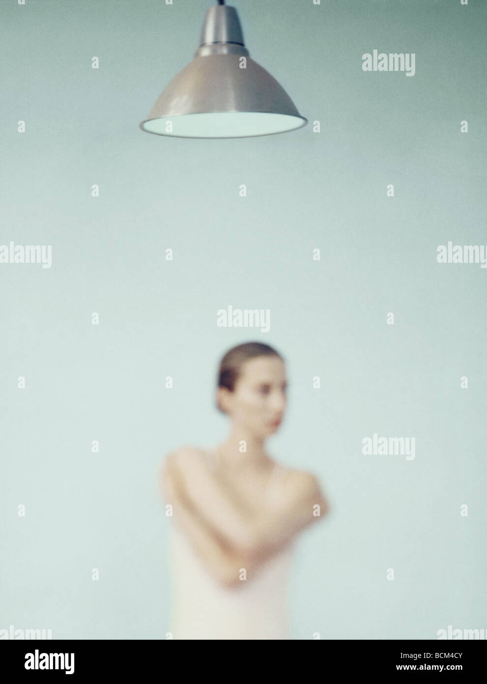 Young woman standing with arms folded, focus on lamp in foreground Stock Photo