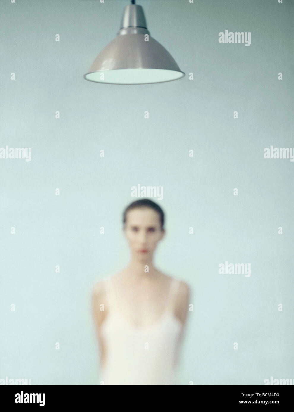 Young woman standing under lamp, focus on lamp in foreground Stock Photo