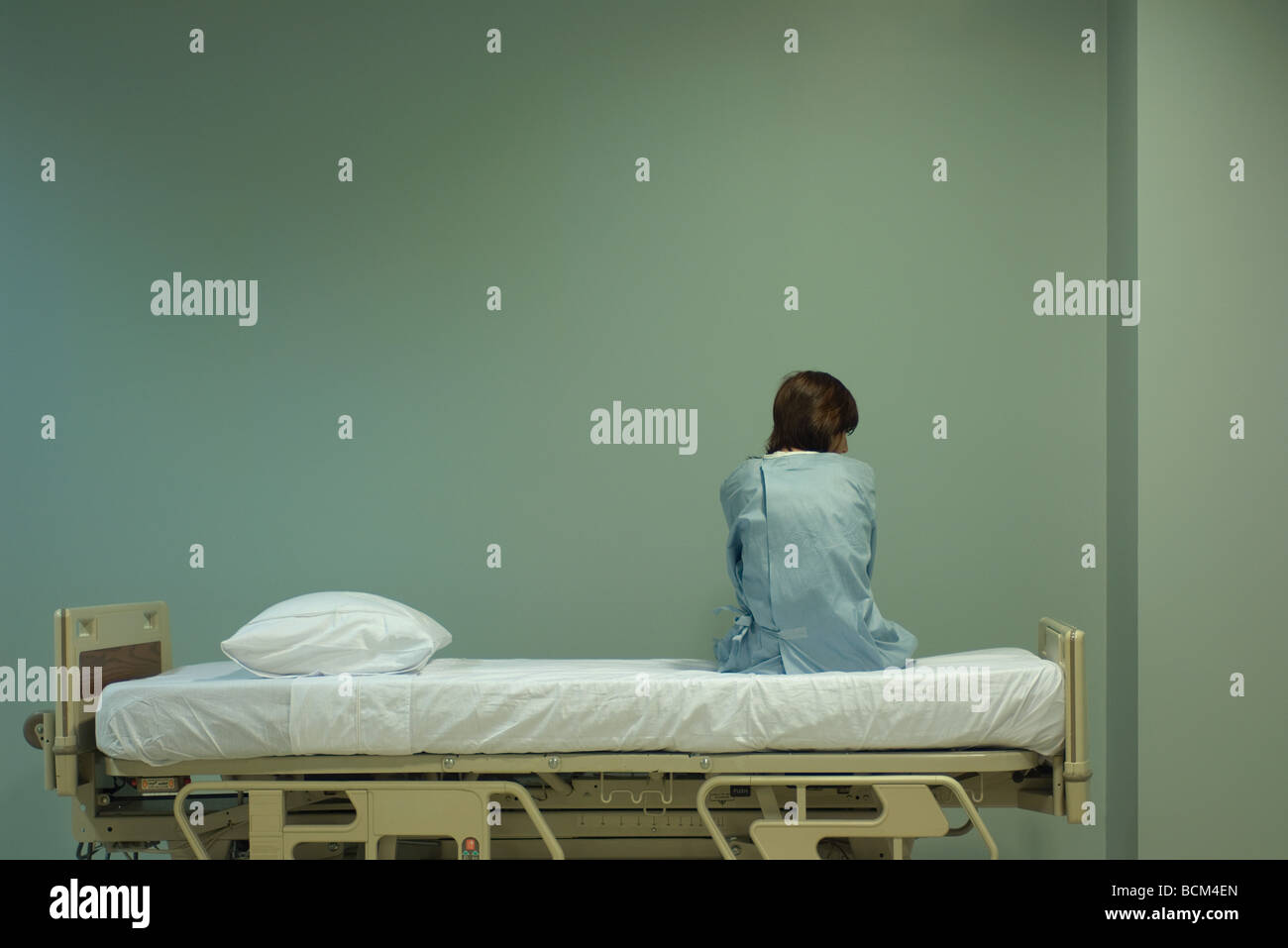 Female patient sitting on hospital bed, rear view Stock Photo