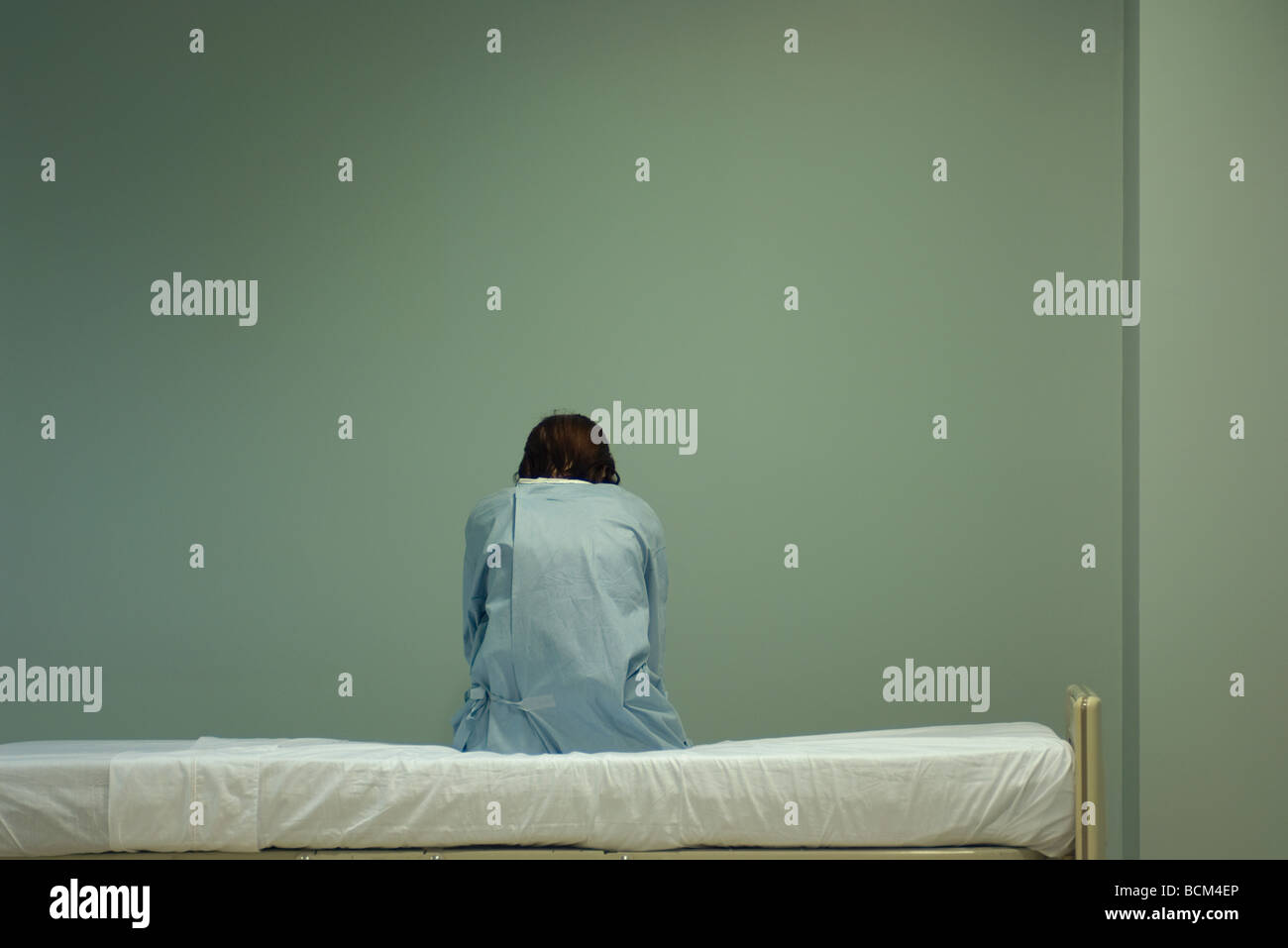 Female patient sitting on hospital bed, head down, rear view Stock Photo