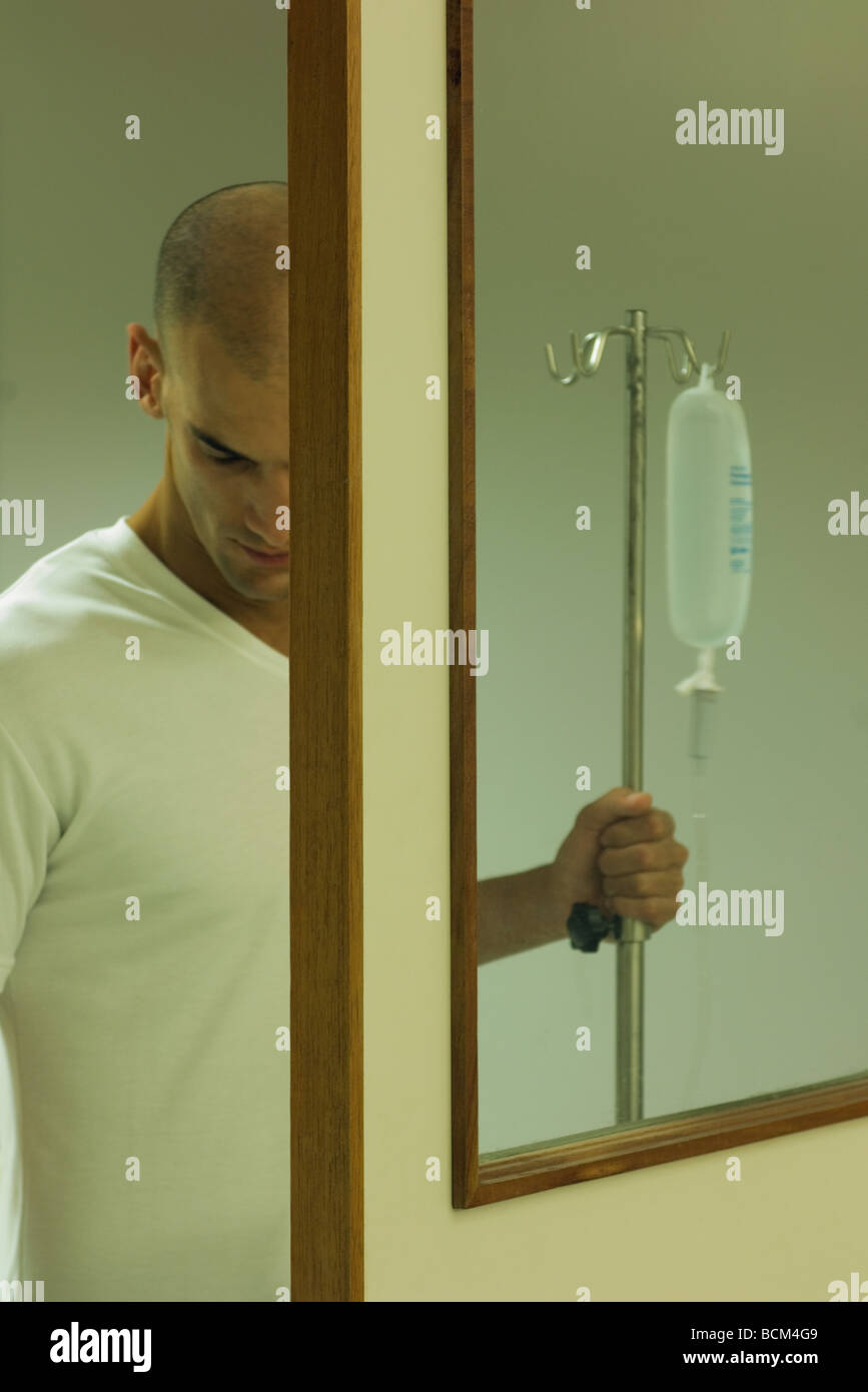 Male patient holding on to IV drip, looking down, viewed through door Stock Photo