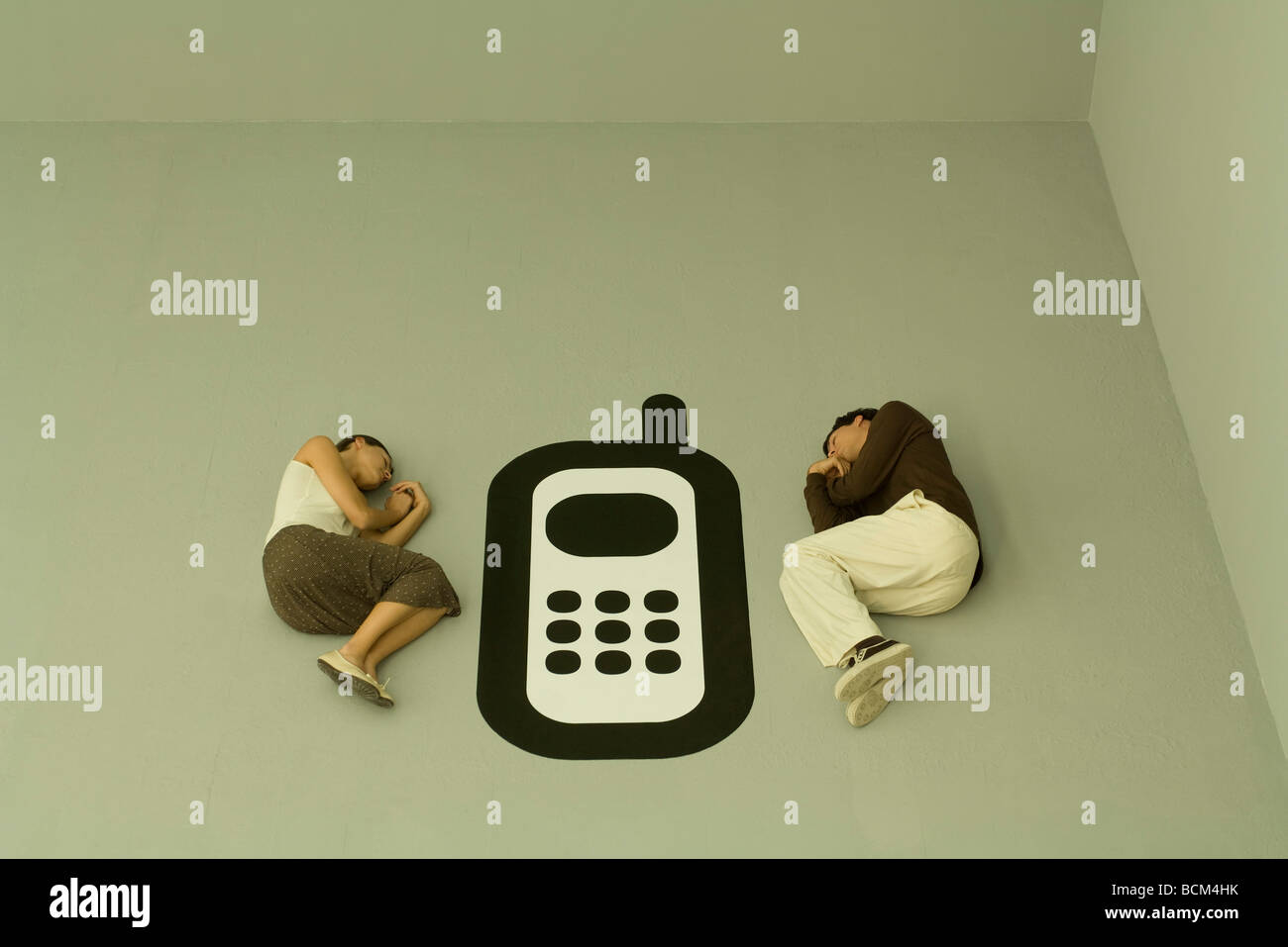 Man and woman lying down on the ground with large cell phone graphic between them Stock Photo