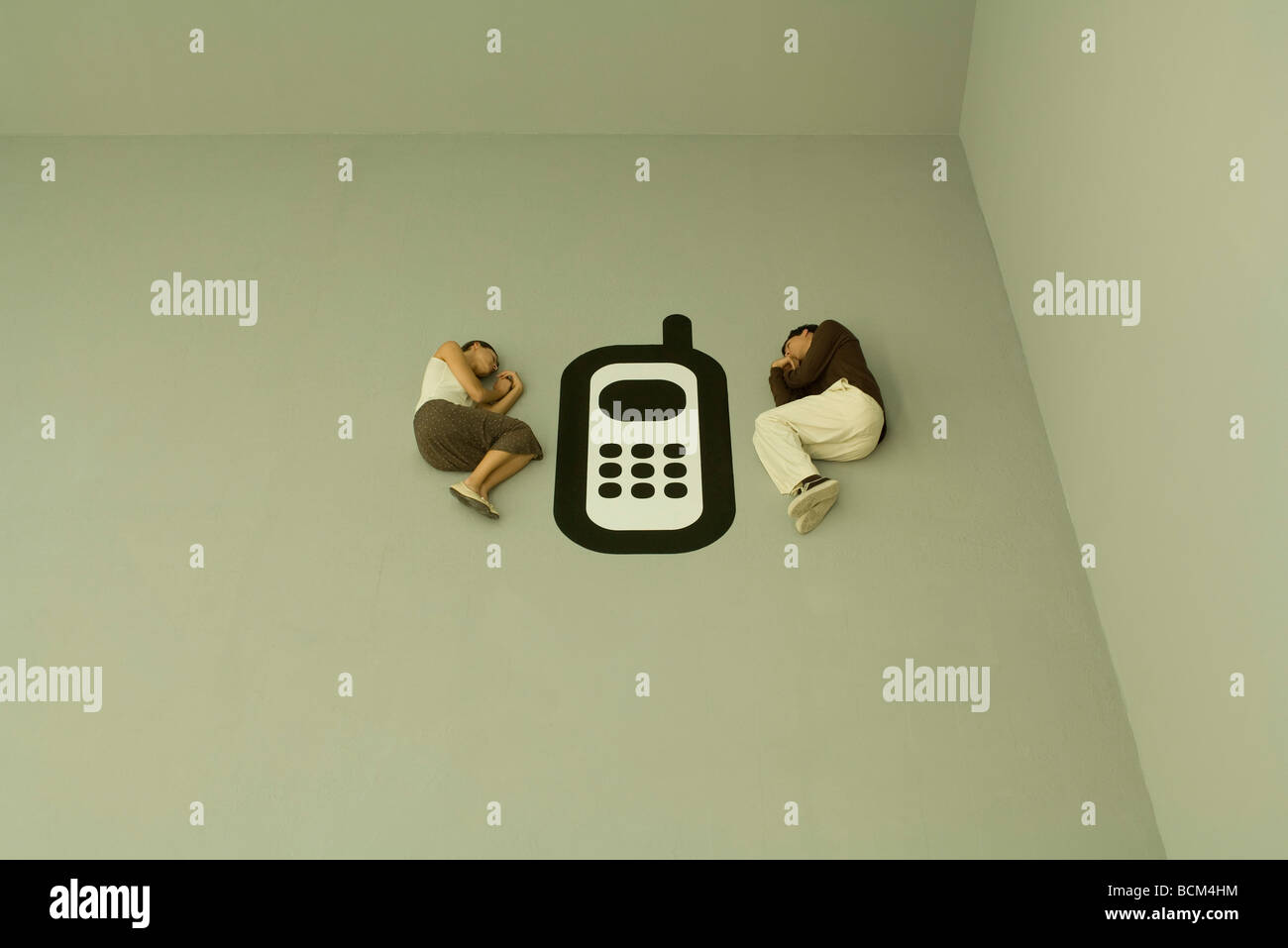 Man and woman lying down on the ground with large cell phone graphic between them Stock Photo