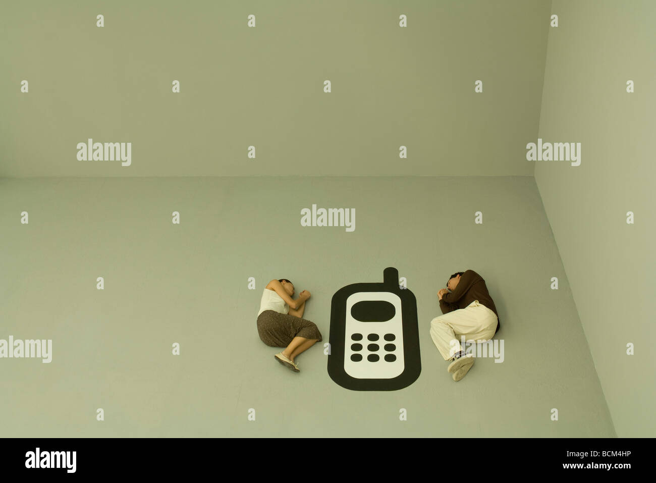 Man and woman lying down on the ground with large cell phone graphic between them Stock Photo