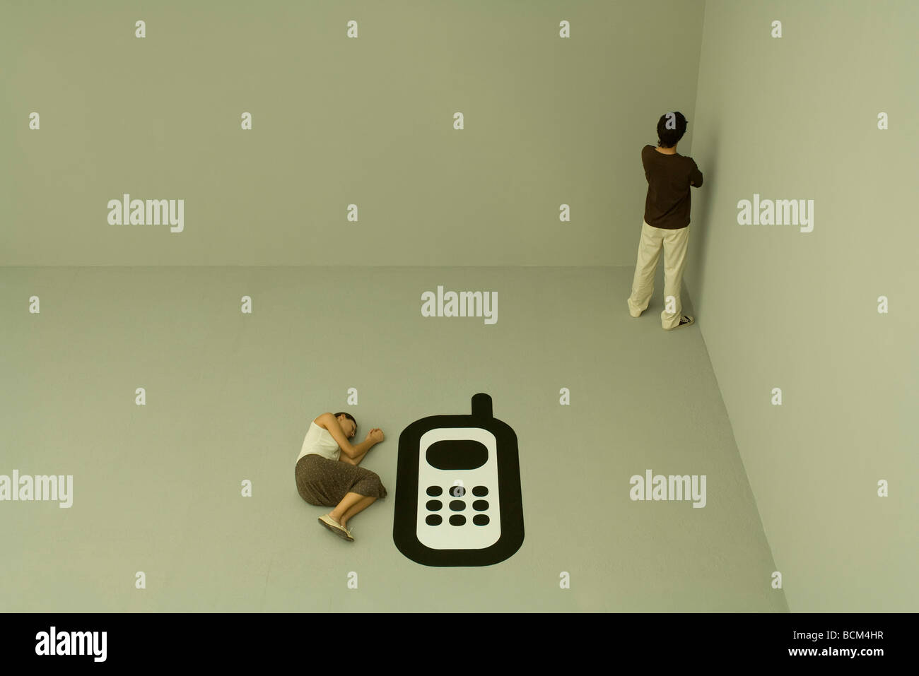 Woman lying on the ground beside large cell phone, man standing in corner Stock Photo