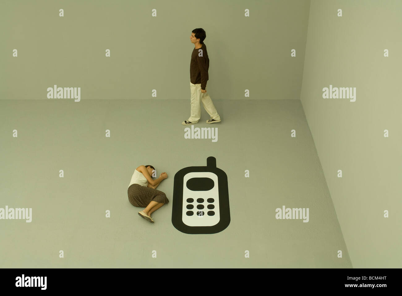 Woman lying down on the ground beside large cell phone, man walking nearby Stock Photo