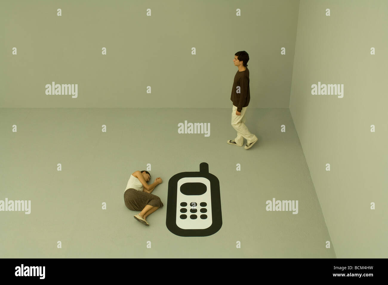 Woman lying down on the ground beside large cell phone, man walking away Stock Photo