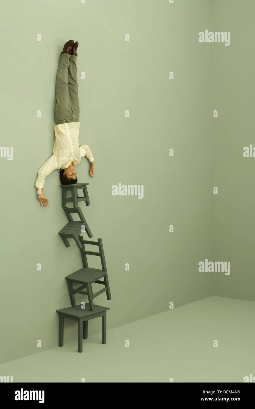 Man doing headstand on top of tall stack of chairs Stock Photo