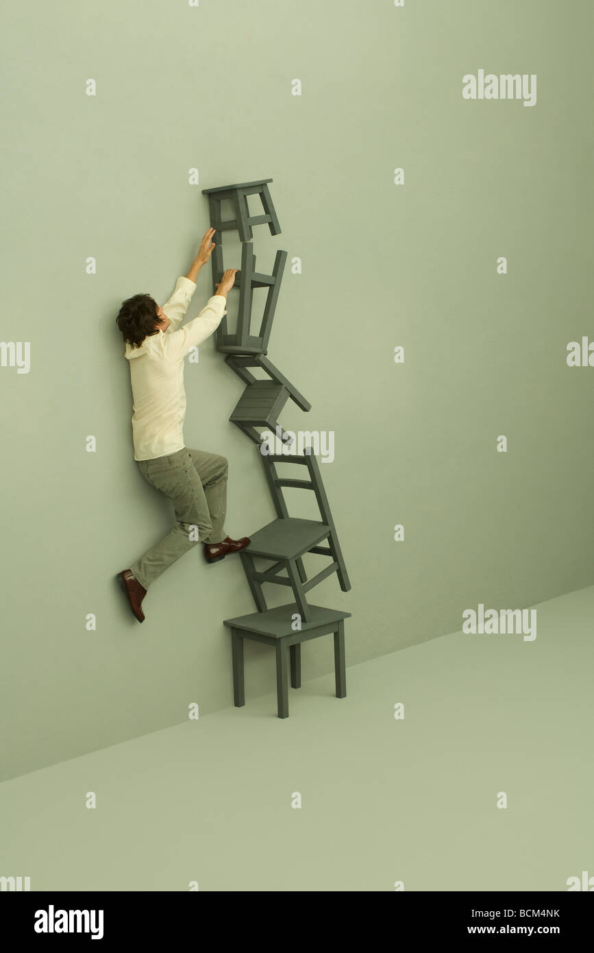 Man climbing precariously stacked chairs Stock Photo Alamy