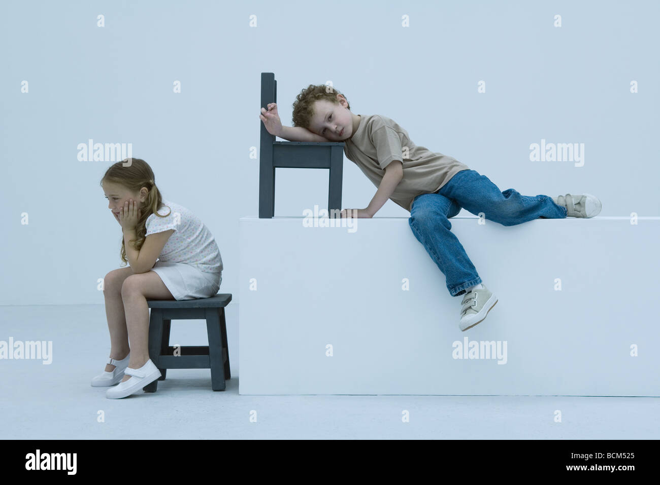 Girl sitting on stool, sulking, brother leaning against chair behind