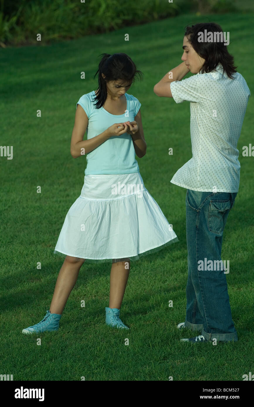 Young couple standing in park, woman looking down at hands Stock Photo
