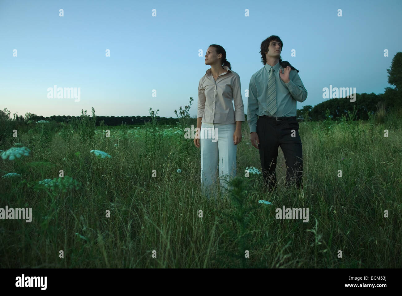 Couple standing in field at dusk, looking in opposite directions Stock Photo