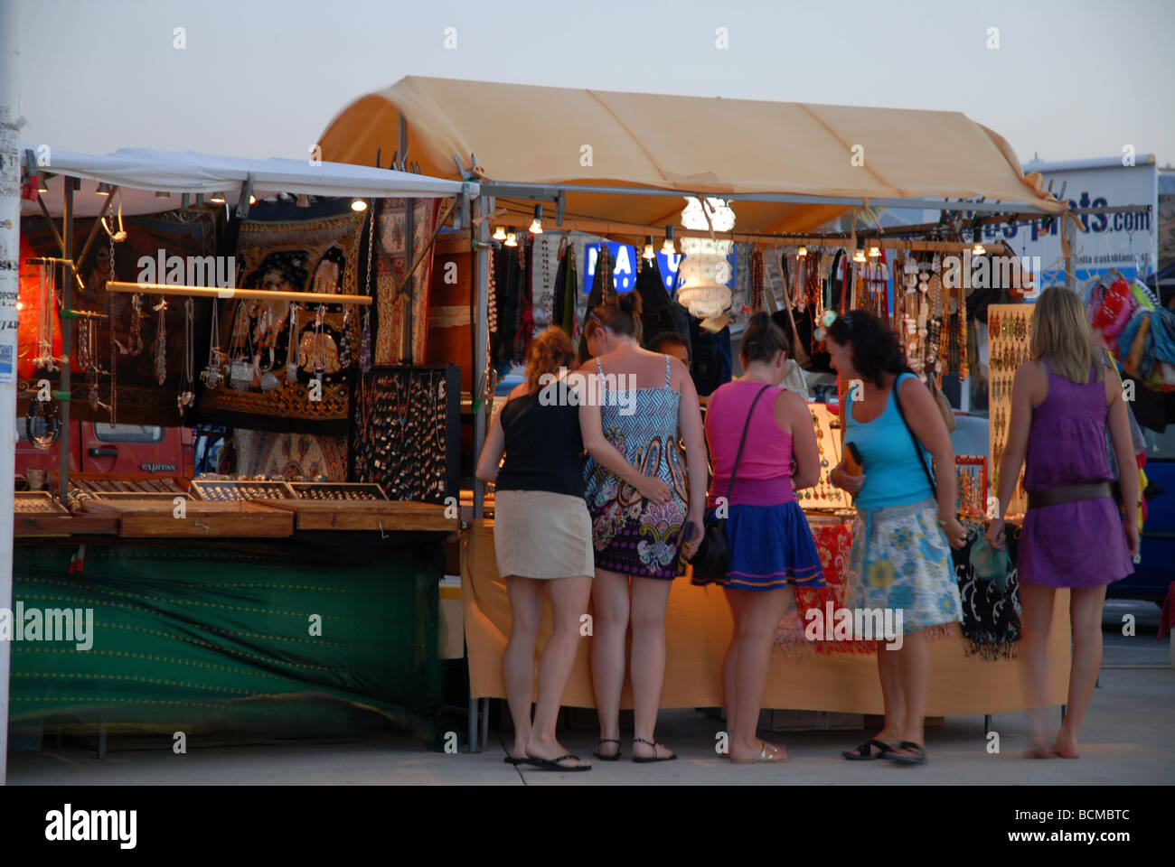 tourists looking at goods for sale on a night market stall at the Arenal, Javea / Xabia, Alicante Province, Spain Stock Photo