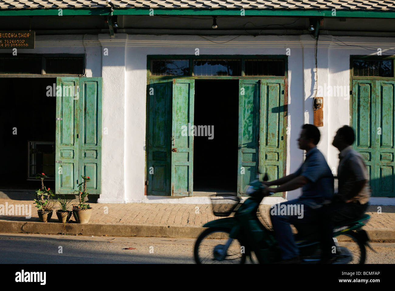 Two men on a moped silhouetted against old colonial buildings in Luangprabang in Laos Stock Photo