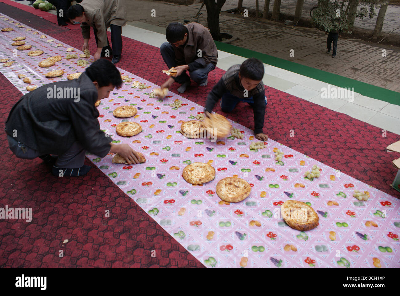 Uyghurs arranging food on carpet, which serves as dinning table in the courtyard of The Id Kah Mosque, Kashgar, Kashgar Stock Photo