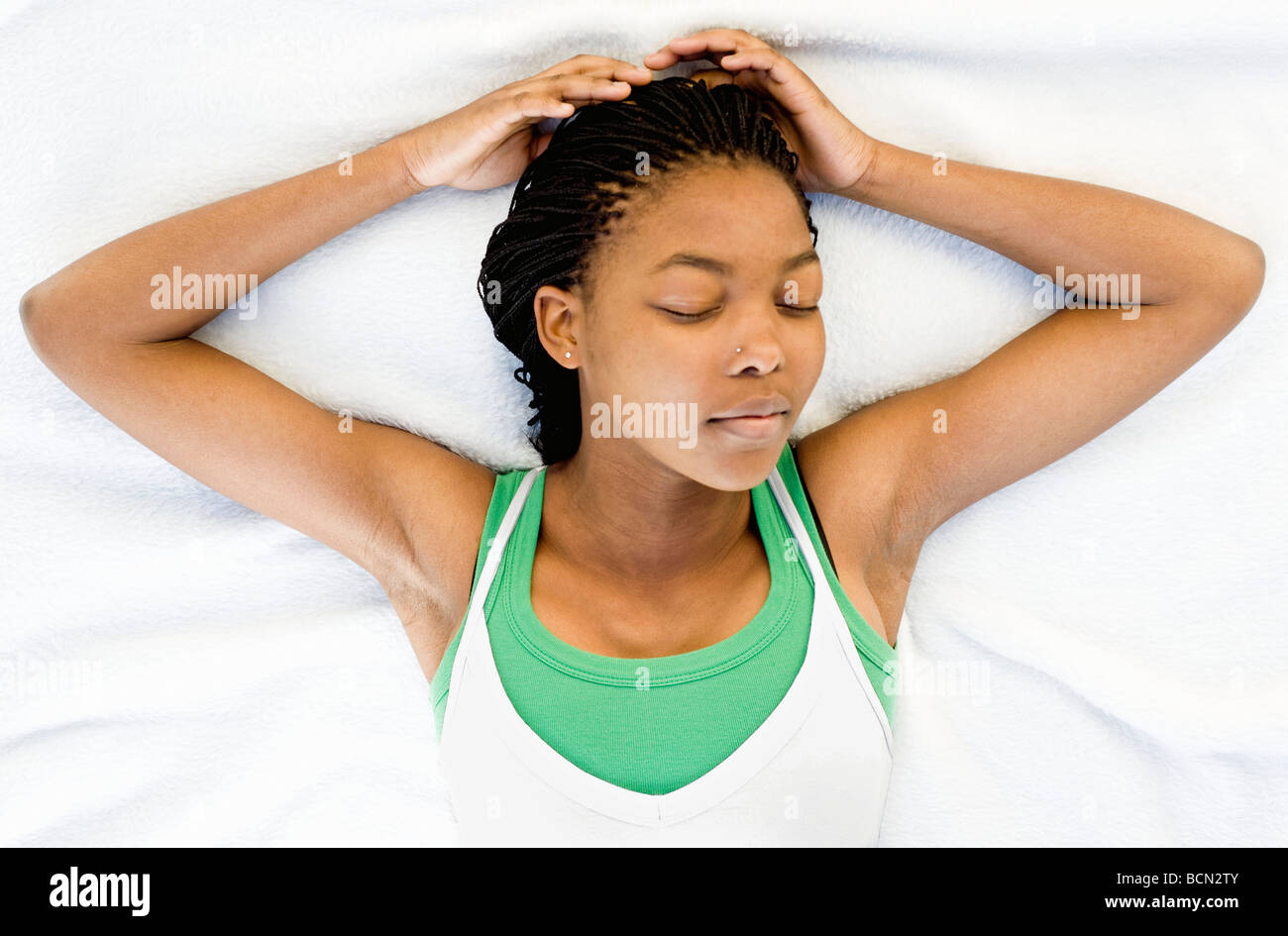 A young woman calmly sleeping on a white blanket with arms upraised Stock Photo