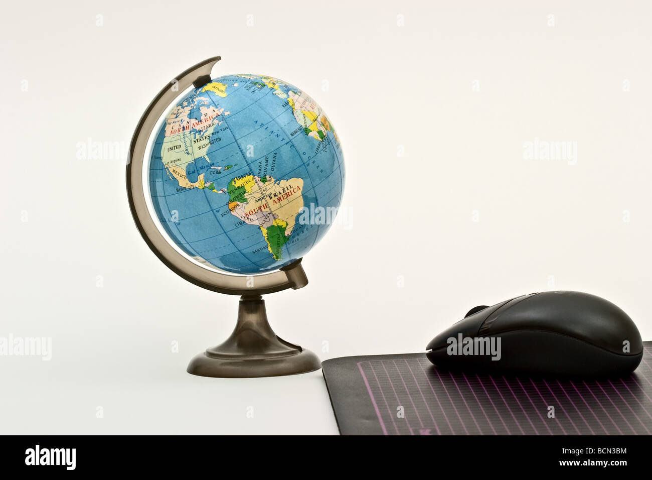 Mouse on a mouse pad pointing towards a plastic globe of the world Stock Photo