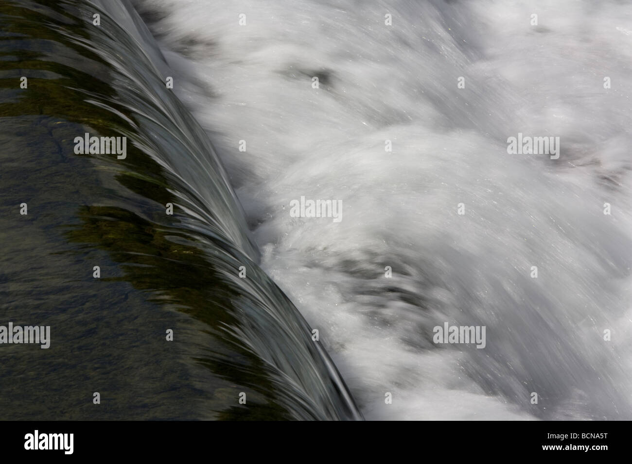 Clear, calm water becomes a mass of white as it cascades over a weir at Lods, Stock Photo