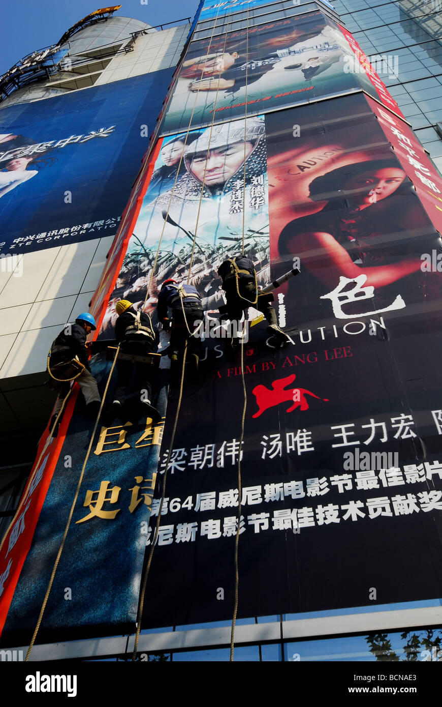 Workers with safety harness taking off large advertisement on the wall of a building, Shanghai, China Stock Photo