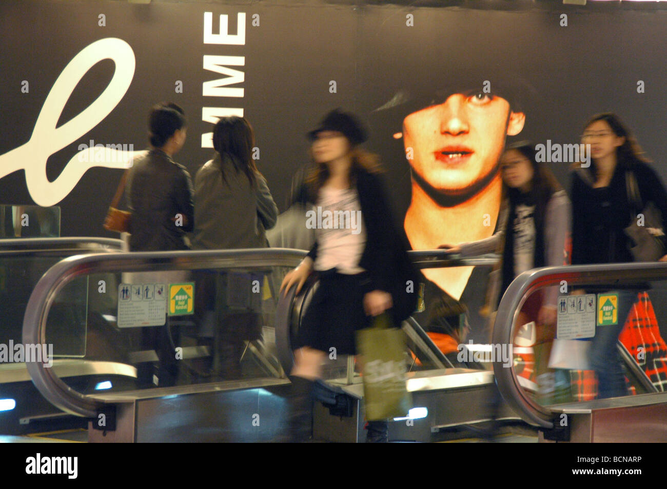 Trendy shoppers walk pass large advertisement in shopping mall, Shanghai, China Stock Photo