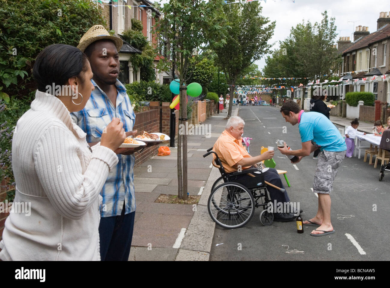Big Lunch Street Party neighbour helping disabled person Black British BAME couple Brunswick Street Walthamstow London E17 UK 2009 2000S HOMER SYKES Stock Photo