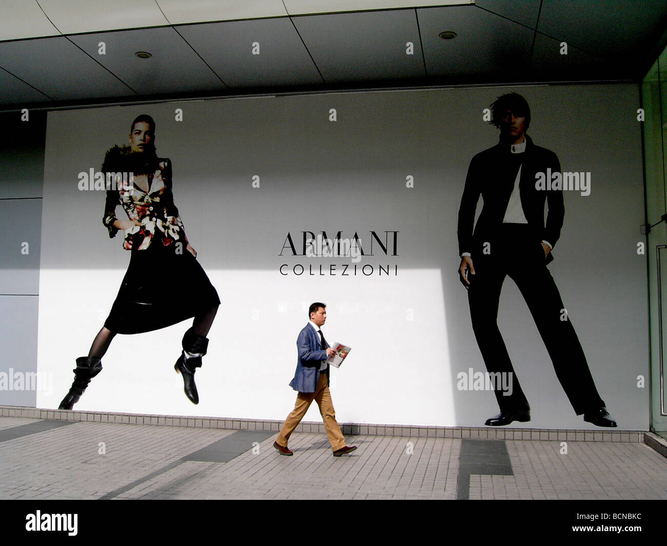 Chinese man walking pass large advertisement for Armani, Shanghai, China Stock Photo