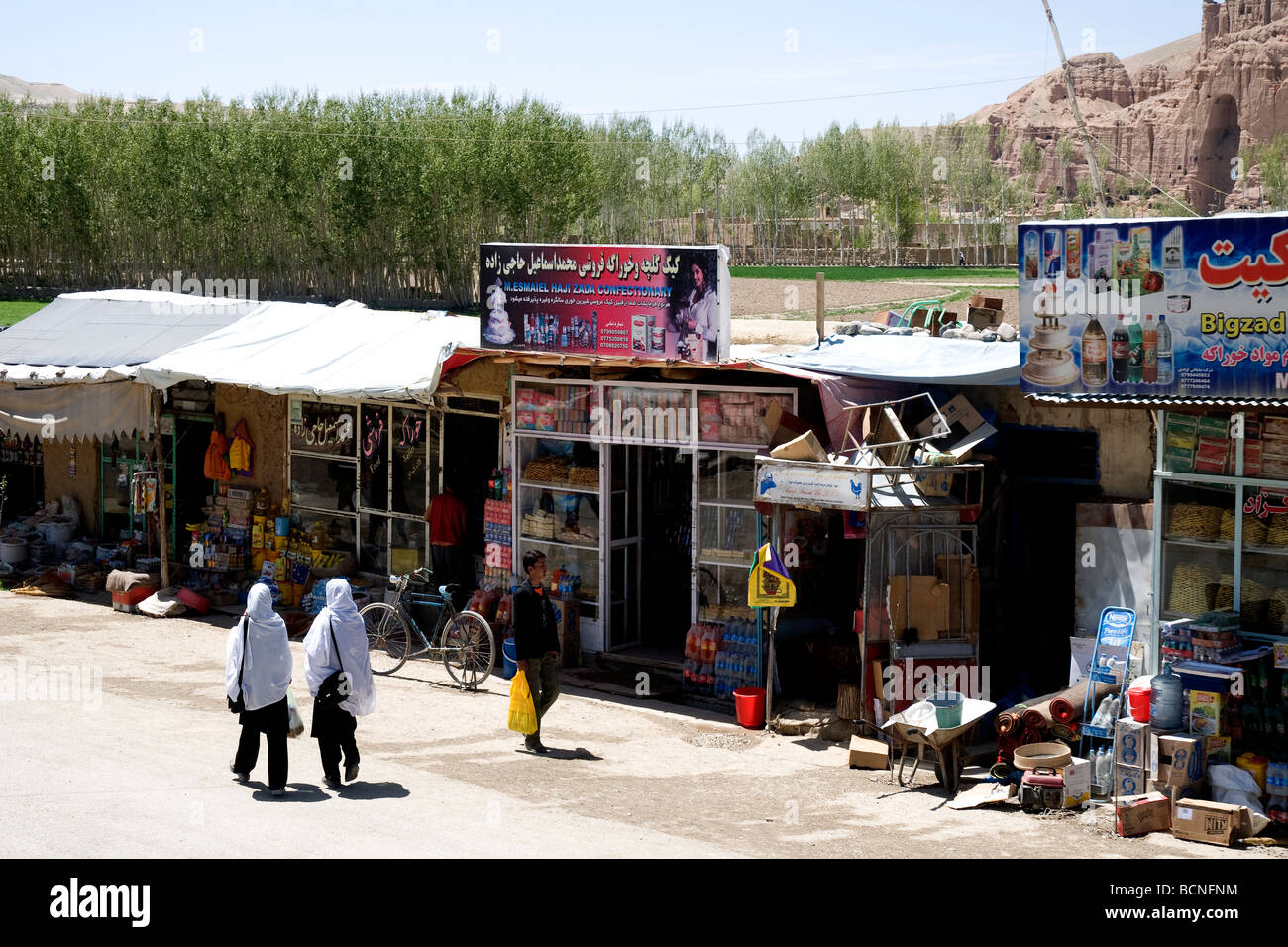 Two white-veiled schoolgirls walk up a street past Bamiyan shops, Afghanistan Stock Photo