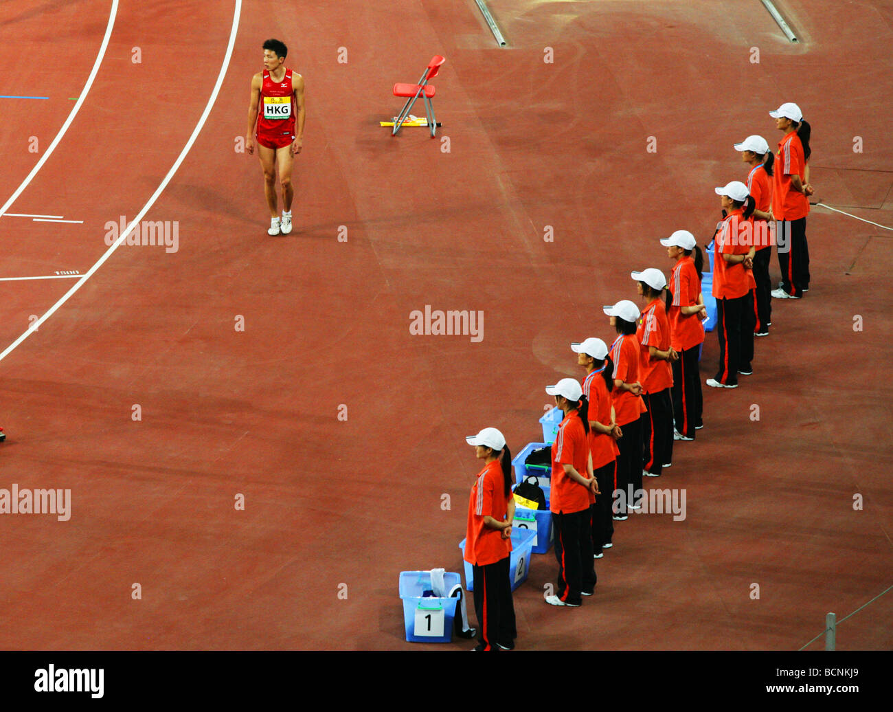 An athelete from Hong Kong walks pass a row of janitors, Beijing, China Stock Photo