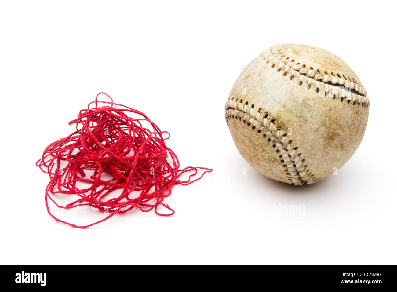 Old baseball with red stitching threads removed and in a pile next to