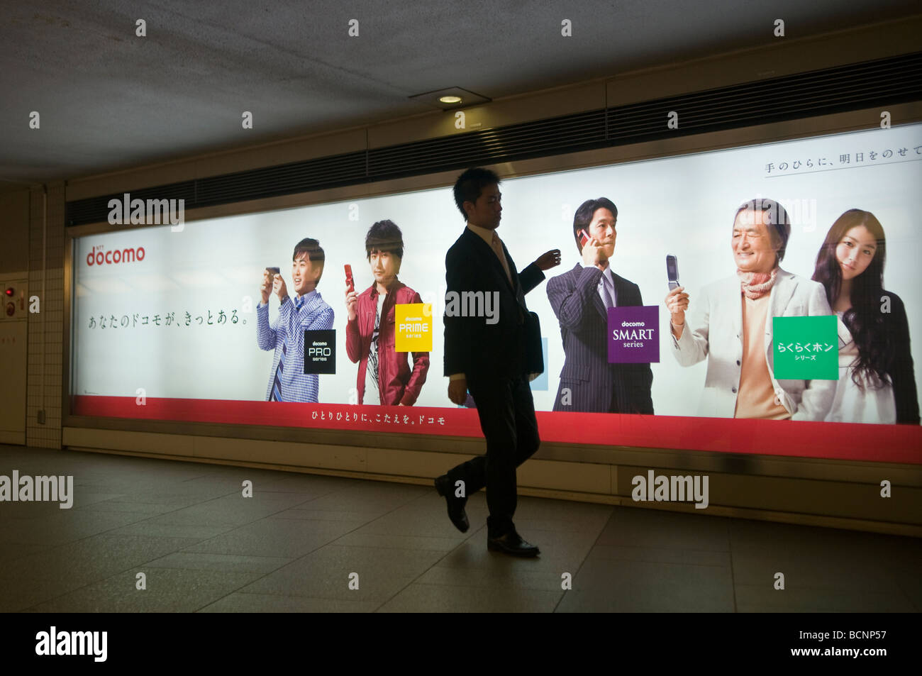 Pedestrian walks past billboard advertising DOCOMO the predominant mobile phone operator in Japan in an underground passage central Tokyo Stock Photo