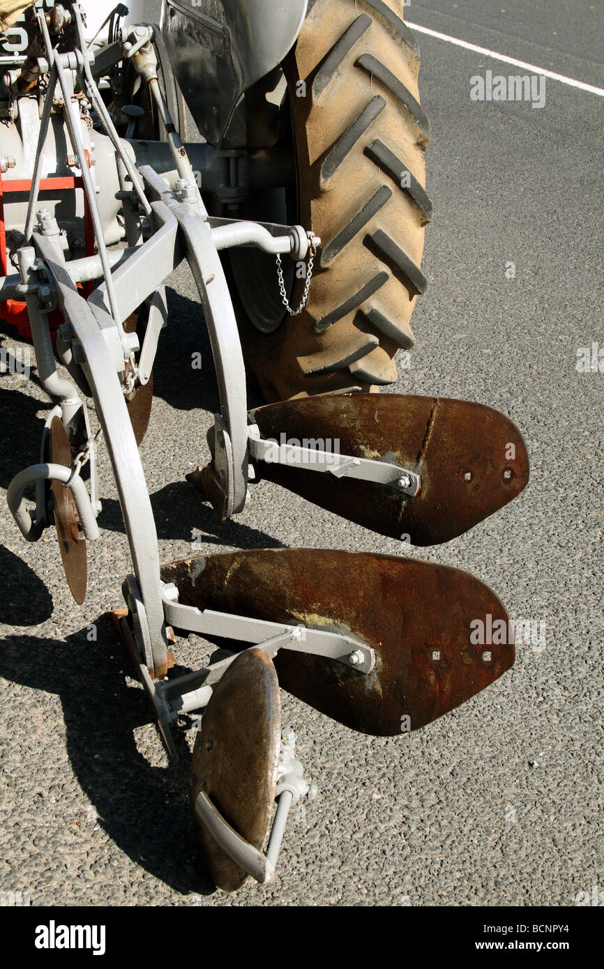 Plough Implement attached to a Vintage Massey Ferguson Tractor used to turn the soil  for agricultural cultivation Stock Photo