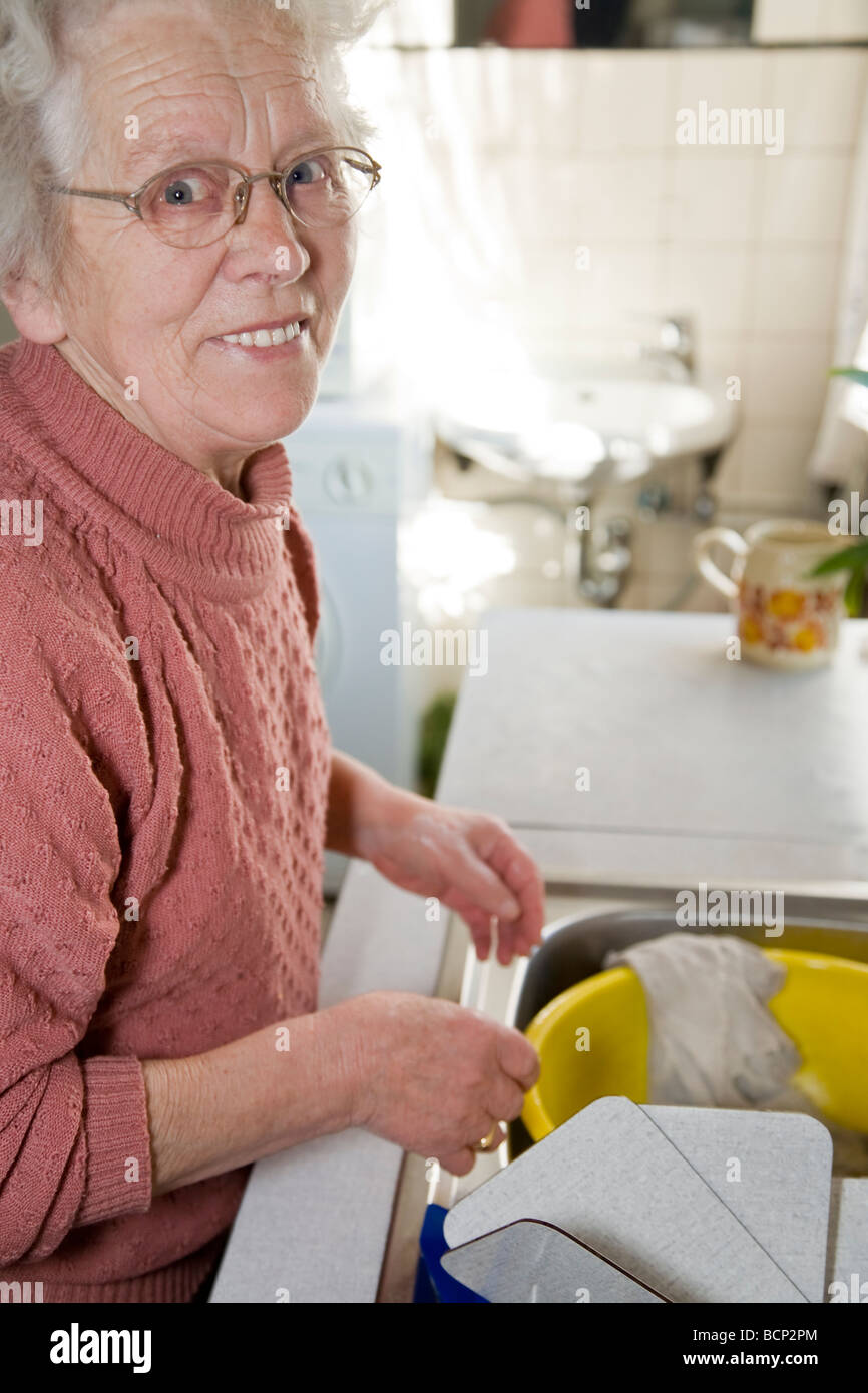 Fröhliche Frau in ihren 70ern wäscht Geschirr in der Küche ab Stock Photo