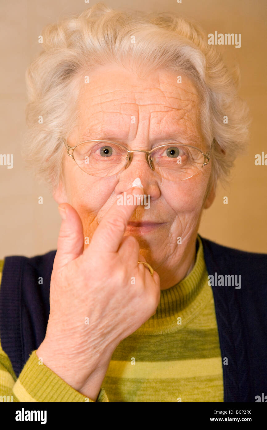 Frau in ihren Siebzigern cremt sich die Nase ein Stock Photo