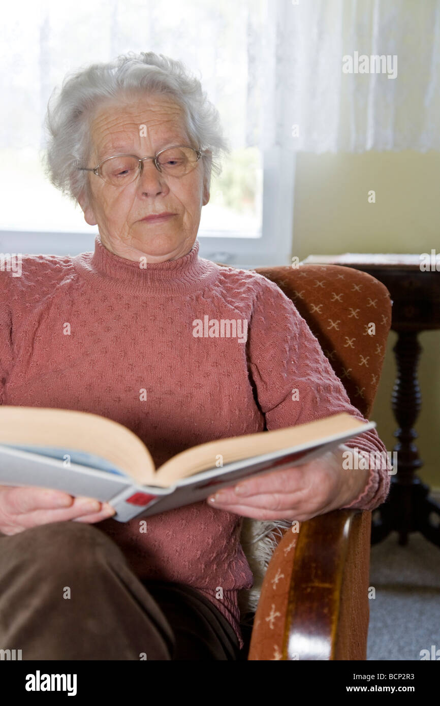 Frau in ihren Siebzigern sitzt in einem Sessel und liest in einem Buch Stock Photo