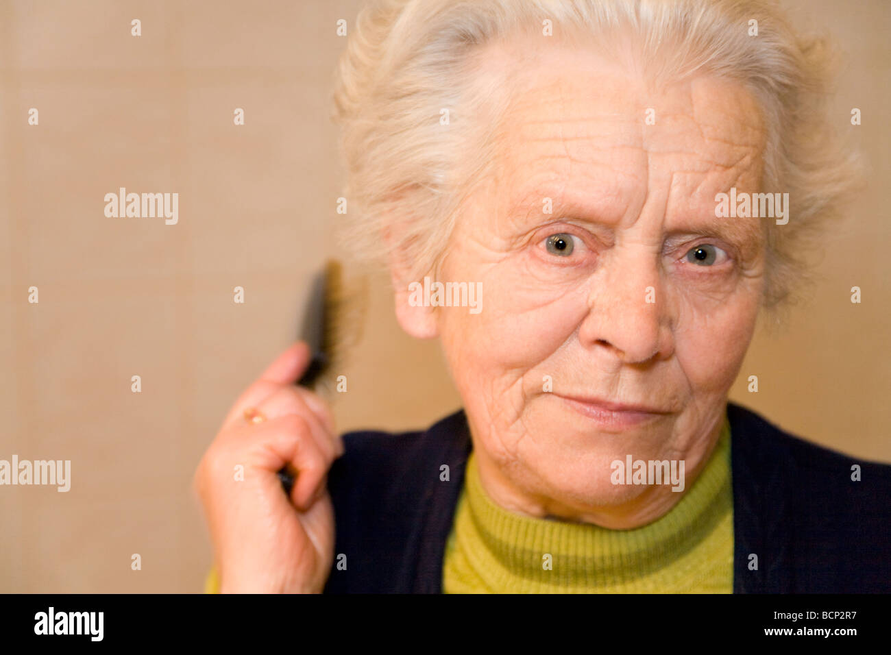 Frau in ihren Siebzigern bürstet sich ihre grauen Haare Stock Photo