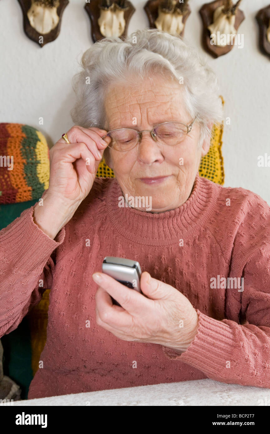 Frau in ihren Siebzigern sitzt auf einem Sofa im Wohnzimmer und hat Probleme etwas auf ihrem Handy zu erkennen Stock Photo