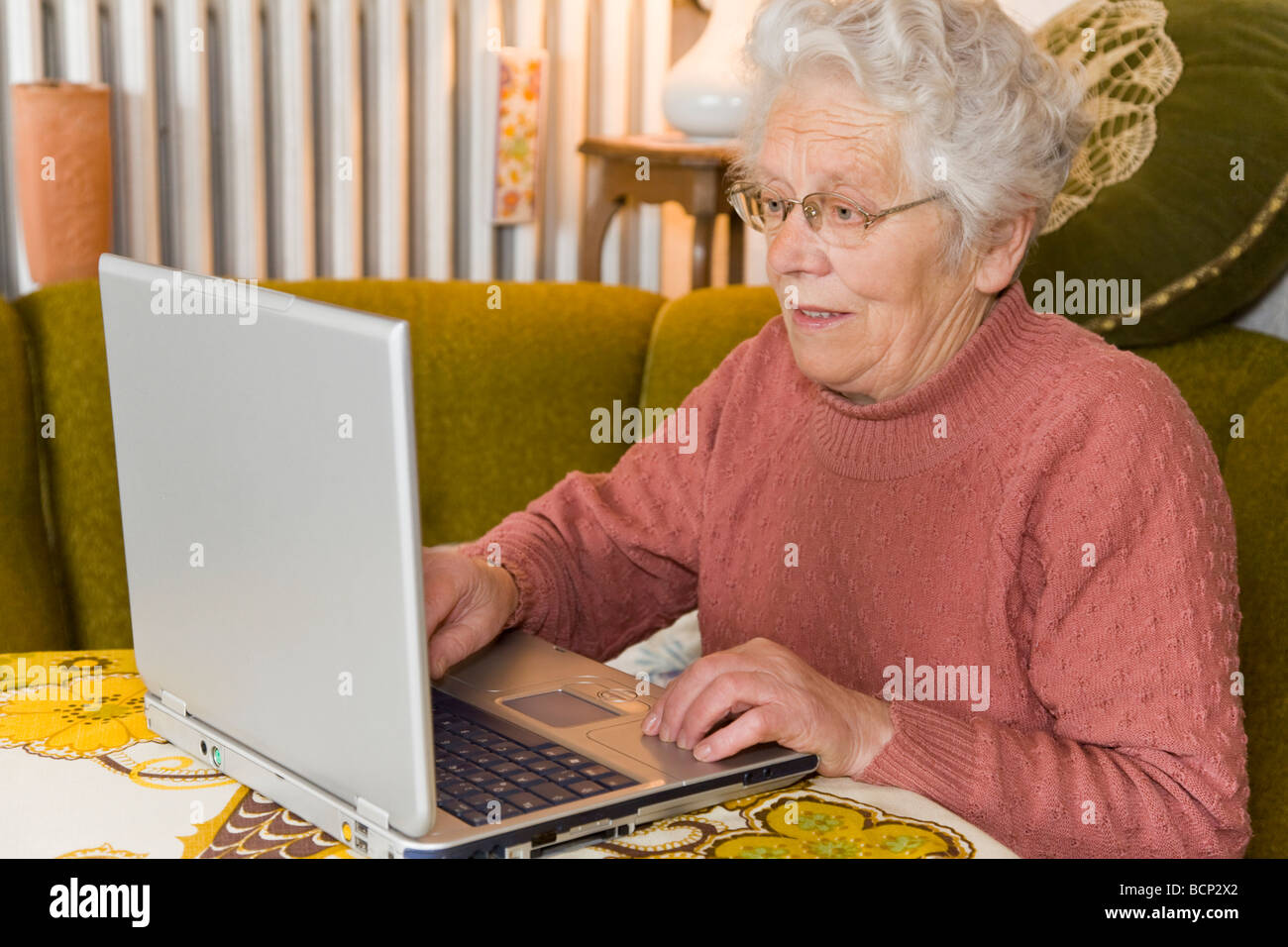 Frau in ihren Siebzigern sitzt im Wohnzimmer am Laptop Stock Photo