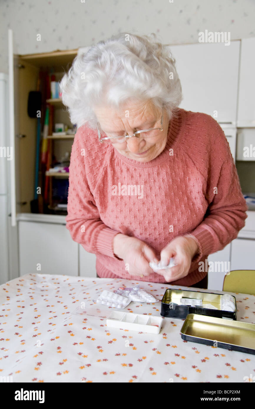 Frau in ihren Siebzigern steht am Küchentisch und sortiert ihre Tabletten in eine Pillendose Stock Photo