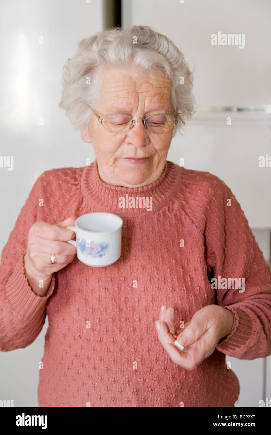 Frau in ihren Siebzigern steht in der Küche und schluckt ihre Tabletten Stock Photo