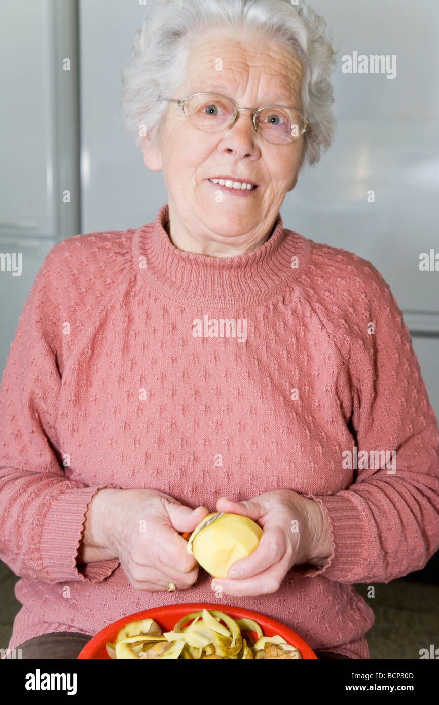 Frau in ihren Siebzigern sitzt in der Küche und schält Kartoffeln Stock Photo