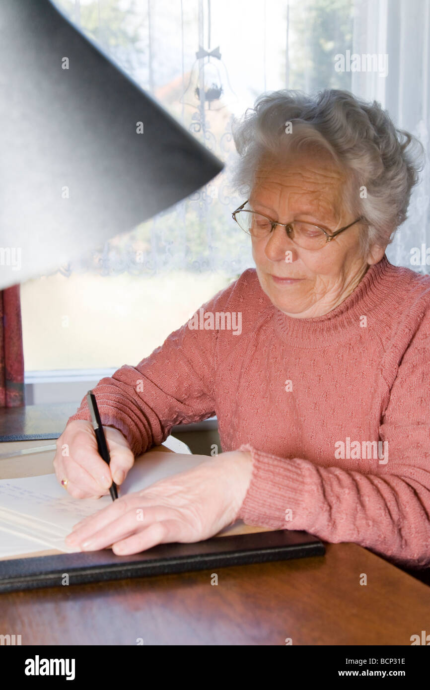 Frau in ihren Siebzigern sitzt am Schreibtisch und schreibt einen Brief Stock Photo